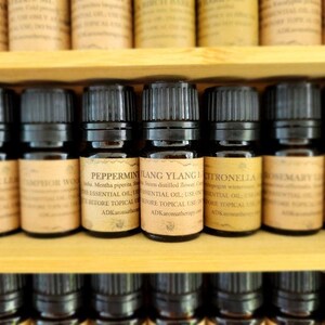 May include: A shelf of small, dark brown glass bottles with black caps, each labeled with a different essential oil name, including Peppermint, Ylang Ylang, Citronella, Rosemary, and  "PING".