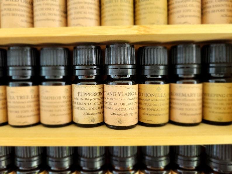 May include: A shelf of small, dark brown glass bottles with black caps, each labeled with a different essential oil name, including Peppermint, Ylang Ylang, Citronella, Rosemary, and  "PING".