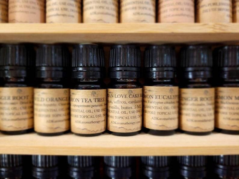 May include: A close-up view of a shelf with small glass bottles filled with essential oils. The bottles have brown labels with white text and are arranged in a row. The labels include names like "Lemon Tea Tree", "Vanilla Love Cake", and "Lemon Eucalyptus".