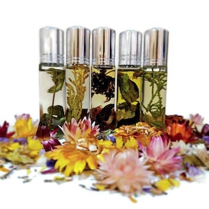 May include: Five small glass bottles with silver roll-on tops filled with a clear liquid and dried flowers. The bottles are arranged in a row on a white surface surrounded by dried flowers in various colors.