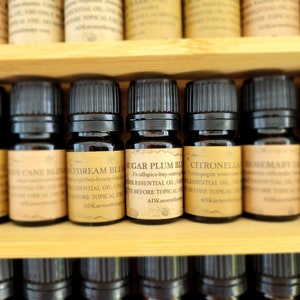 May include: A wooden box filled with small glass bottles of essential oils. The bottles have black caps and labels with names like "Sugar Plum Blend", "Citronella", and "Rosemary".