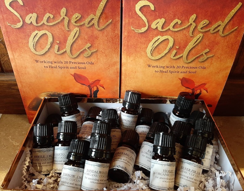 May include: A box filled with small brown glass bottles containing essential oils. The bottles are labeled with names like "Mystle", "Santo", "Jandalwood", and "Jarrow". The box is sitting in front of two books titled "Sacred Oils: Working with 20 Precious Oils to Heal Spirit and Soul."