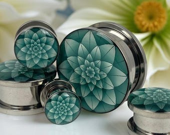 May include: A collection of teal and silver ear plugs with a floral design. The plugs are displayed on a white surface, with white flowers in the background. The plugs vary in size.