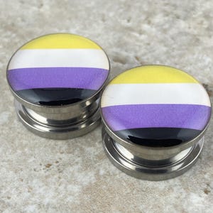 May include: A pair of stainless steel ear gauges with a black, purple, white, and yellow design. The design is reminiscent of the non-binary pride flag.