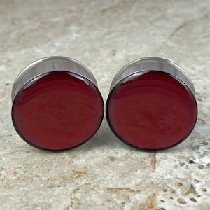 May include: Pair of red and silver ear gauges. The gauges have a smooth, shiny finish and a red center.