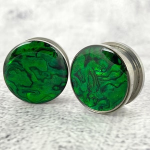 May include: A pair of green abalone shell ear gauges with a silver metal rim. The gauges have a swirling green pattern.