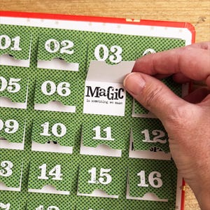 Puede incluir: Un calendario de adviento verde y blanco con solapas numeradas. La solapa del d&iacute;a 3 est&aacute; abierta, revelando una tarjeta blanca con el texto "MaGic is something we make".