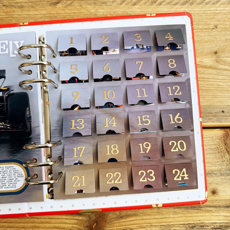 Puede incluir: Un calendario gris y dorado con 24 solapas numeradas. Cada solapa tiene un n&uacute;mero dorado sobre un fondo gris. El calendario est&aacute; abierto para revelar los n&uacute;meros del 1 al 24.
