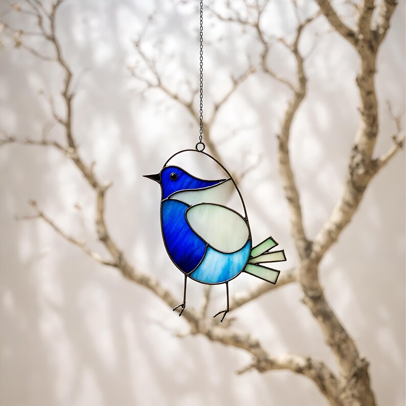 May include: A stained glass bird ornament with blue, white, and green glass pieces. The bird is hanging from a silver chain.