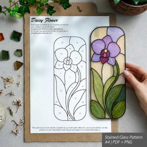 May include: A stained glass pattern for an orchid flower on A4 paper, featuring a numbered line drawing and a finished rectangular glass panel with purple petals, a yellow centre, and green leaves, labelled Daisy Flower.