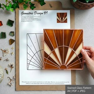Può includere: Un pannello quadrato in vetro colorato con un motivo a raggiera nei toni dell'ambra e della crema, costruito con linee in lamina di rame. Il pannello è mostrato sopra un modello di carta A4 stampato etichettato Geometric Design VI con sezioni numerate.