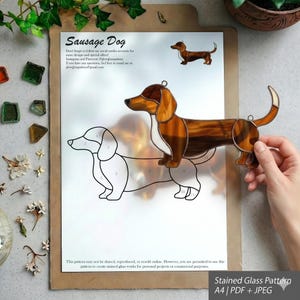 Pode incluir: Um padrão de vitral com um design de cão salsicha. O padrão inclui uma peça de vidro acabada em castanho, branco e âmbar, e um desenho a traço. O texto "Sausage Dog" está no topo.