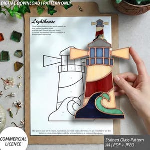 Könnte beinhalten: Eine digitale Vorlage für ein Buntglas-Leuchtturm-Muster, bestehend aus einer gedruckten Strichzeichnung auf Papier und einem fertigen Leuchtturm-Objekt aus roten, cremefarbenen und blauen Glassegmenten mit Lichtstrahl- und Wellendesign.