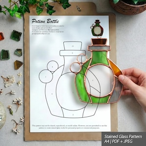 Può includere: Un modello per vetrate artistiche raffigurante una boccetta di pozione su un foglio di carta bianco, con un disegno a linee numerate e un pezzo di vetro verde e ambra parzialmente assemblato con bordi in rame, etichettato Potion Bottle e Stained Glass Pattern.