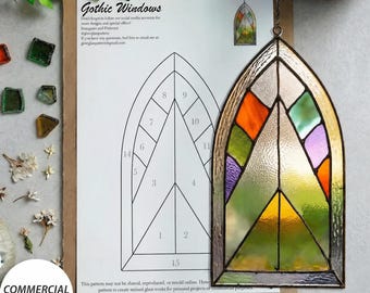 Könnte beinhalten: Ein digitales Download-Muster für ein gotisches Fenster aus Buntglas, bestehend aus einer nummerierten Strichzeichnung auf Papier und einer fertigen Buntglasscheibe mit orangefarbenen, grünen, violetten und gelben Glassegmenten, die durch dunkle Metalllötstellen verbunden sind.