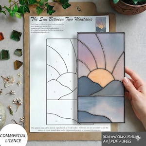 May include: A rectangular stained glass panel depicting a sunrise over mountains and water, featuring pastel pink, orange, and blue glass segments joined by dark metal solder lines, displayed alongside a printed A4 paper pattern template.