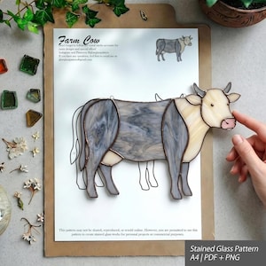 Könnte beinhalten: Ein Kuh-Sonnenfänger aus Buntglas mit cremefarbenem Kopf und Hals sowie einem grau marmorierten Körper. Das Stück liegt auf einer gedruckten Papiervorlage mit der Aufschrift Farm Cow, die eine kleine Kuh-Illustration und Text enthält.