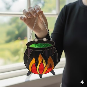 May include: A stained glass cauldron with a silver chain for hanging. The black cauldron has a green liquid inside and flames in shades of red, orange, and yellow at the bottom. The cauldron is a Halloween decoration.