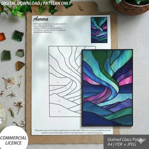 May include: A stained glass pattern titled "Aurora" with a digital download option. The pattern includes a color guide and a black and white outline. The finished artwork depicts a colorful aurora borealis scene with blues, greens, and purples. The pattern is A4 size and comes in PDF and JPEG formats.
