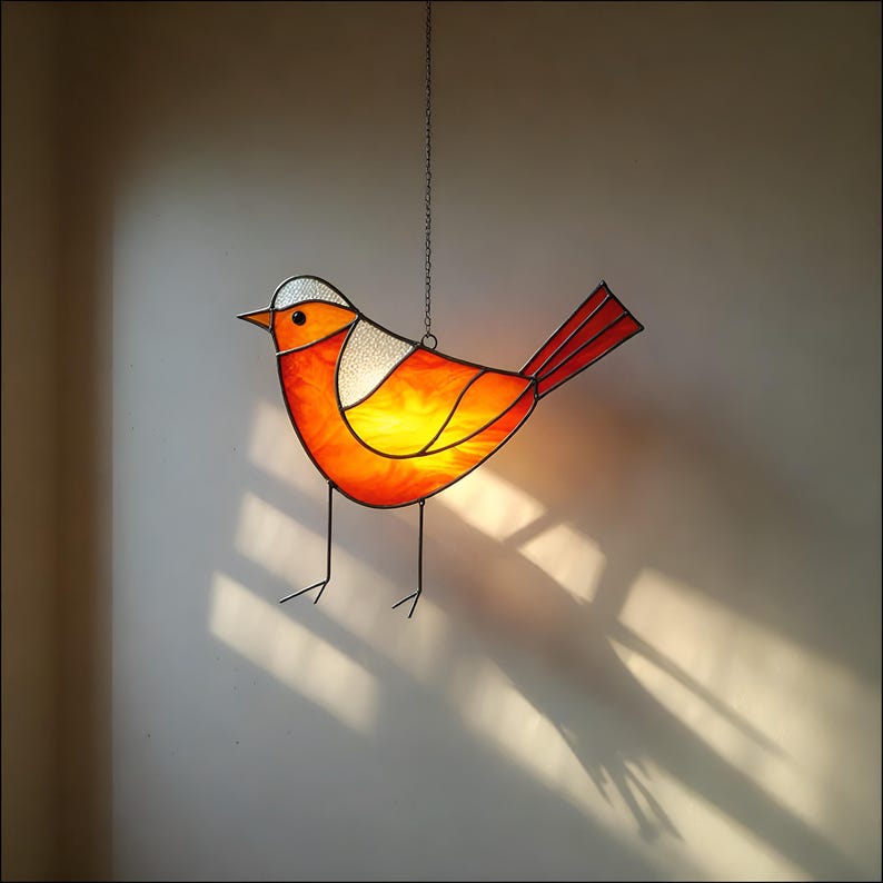 May include: A stained glass bird with orange, red, and white glass panels. The bird is hanging from a chain and is casting a shadow on the wall.