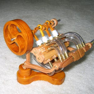 May include: A wooden model of a four-cylinder engine with clear plastic tubing and a wooden flywheel. The engine is mounted on a wooden base.