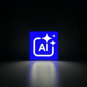 May include: A square blue sign featuring a white graphic icon of a rounded rectangle containing the letters AI, accompanied by three four-pointed star shapes of varying sizes positioned above and to the right of the text, all glowing brightly.
