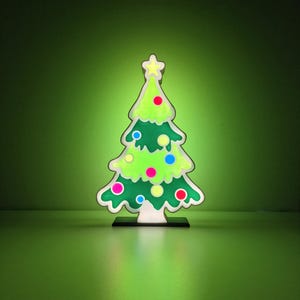 Peut inclure: Décoration de sapin de Noël fantaisiste avec un corps vert vif, des bordures blanches et des ornements colorés. L'arbre est surmonté d'une étoile jaune et repose sur une base noire. Le design est souligné en blanc, créant une esthétique ludique et cartoon.