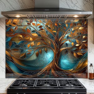 May include: A kitchen splashback with a stained-glass effect tree design. The artwork uses gold, brown, blue, and orange hues. The tree's branches and leaves are detailed. The splashback is likely made of glass and is mounted behind a hob.