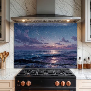 Puede incluir: Un protector de salpicaduras de vidrio con una serena escena oceánica bajo un cielo estrellado. La obra de arte representa olas, nubes y un reflejo brillante. El protector de salpicaduras está instalado detrás de una cocina de gas negra.