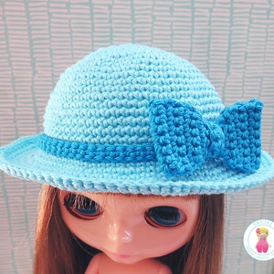 May include: A light blue crocheted hat with a matching blue bow. The hat has a wide brim and is made with a textured stitch.