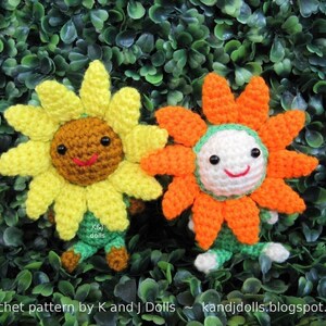 May include: Two crocheted sunflower dolls with smiling faces. One is yellow and brown, the other is orange and white. Both have green and brown accents. The dolls are set against a backdrop of green foliage. The text "Crochet pattern by K and J Dolls" is visible.