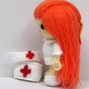 May include: A crocheted doll dressed as a nurse with a white dress, red crosses on her hat, and long orange hair.