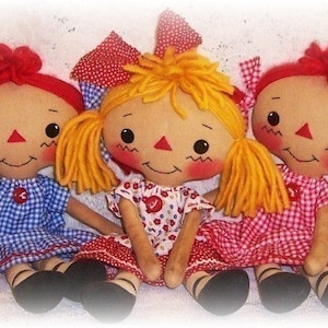May include: Three handmade rag dolls with red hair and gingham dresses. The dolls are sitting on a white background.