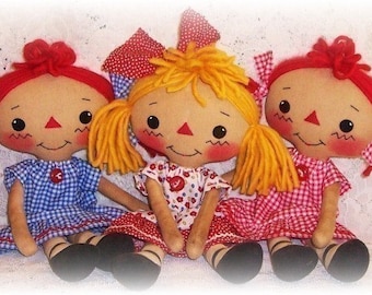 May include: Three handmade rag dolls with red hair and gingham dresses. The dolls are sitting on a white background.