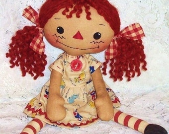 May include: A handmade rag doll with red yarn hair, a red and white gingham bow, and a beige dress with a colourful print of animals and the word "Bunny".