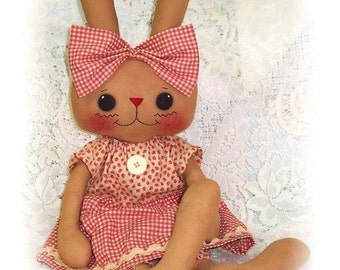 May include: A brown bunny doll with a red and white gingham bow, wearing a pink and white gingham dress with a white button.