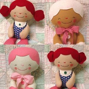 May include: Four handmade fabric dolls with red, pink, and white hair. The dolls are wearing colorful dresses with floral patterns and red and white gingham accents. The dolls have smiling faces with embroidered details.