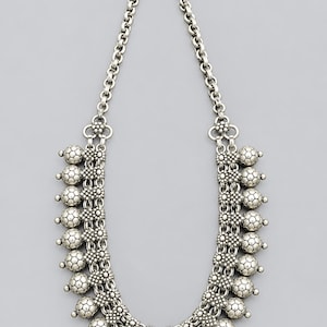 May include: A silver-toned metal necklace featuring a thick chain link design. The lower portion is adorned with multiple rows of textured, spherical beads and small, intricate floral-shaped metal connectors, finished with a simple hook clasp.