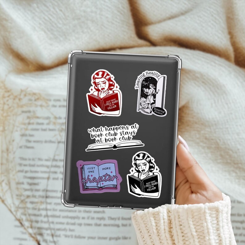 May include: A black e-reader with five stickers on it. The stickers are all black and white and feature illustrations of women reading books. The text on the stickers reads "What happens at book club stays at book club", "Just one more chapter", "But I fell hard for the villain", and "Leaving Reality - Entering Fiction".