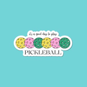May include: A sticker featuring five pickleballs in yellow, pink, and green, with the text "it's a good day to play" above and "PICKLEBALL" below. The sticker has a white border and is set against a teal background.