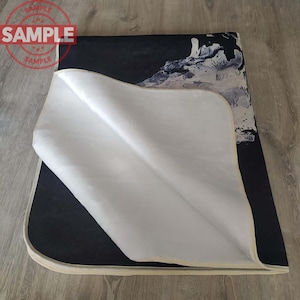Puede incluir: Una alfombra de tela con un dise&ntilde;o abstracto en blanco y negro impreso sobre un fondo blanco. La alfombra tiene un borde de color crema.