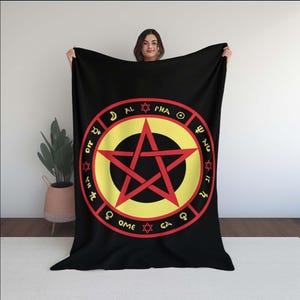 May include: Black blanket featuring a red pentagram inside a yellow circle, surrounded by symbols and text. The blanket is held up, showcasing the design's details. The blanket is a soft, cozy item.