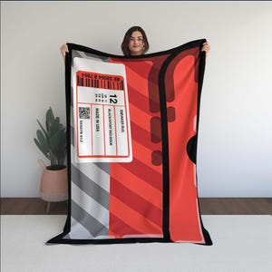 May include: A red and black sneaker rug with a white label that reads "SNEAKER RUG" and "MADE IN USA". The rug has a size 12 label. The rug is held up by a person.