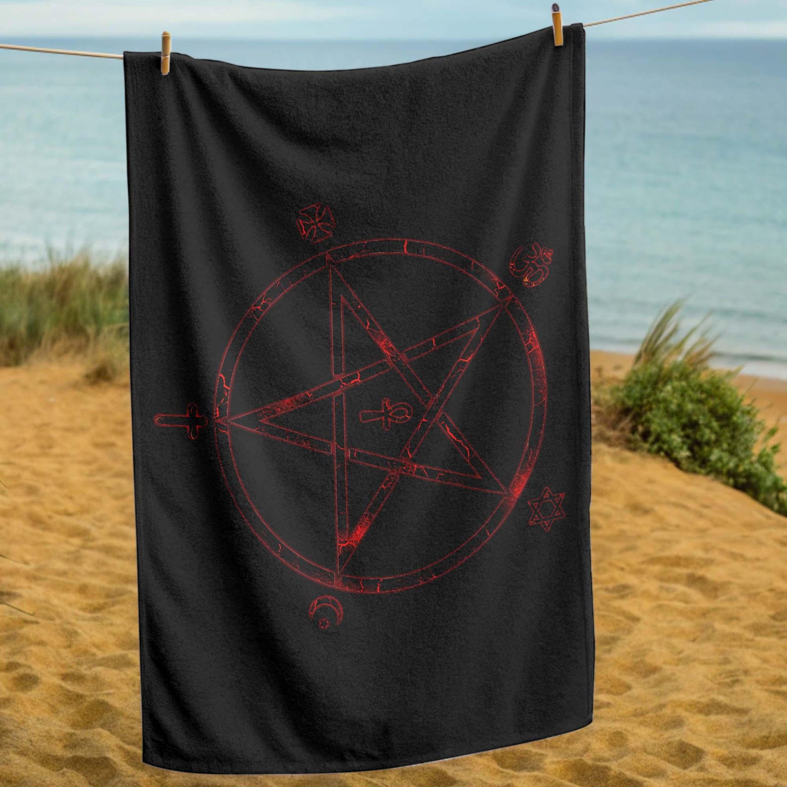 Black beach towel with distressed red occult pentagram and mystical symbols, hanging on clothesline at the beach.