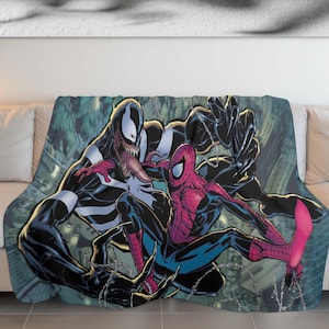 Puede incluir: Una manta de forro polar negra y roja con una imagen de estilo cómic de Venom y Spider-Man luchando. El fondo es verde oscuro y azul con un diseño de telaraña.