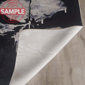 Puede incluir: Una alfombra de arte abstracto en blanco y negro con un respaldo blanco. La alfombra tiene un aspecto desgastado y est&aacute; hecha de un material suave y mullido.