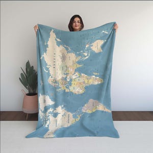 Può includere: Una grande coperta blu con mappa del mondo dall'estetica vintage. La coperta mostra una mappa dettagliata del mondo, con paesi in vari colori. La coperta è tenuta in alto, mostrando le sue dimensioni e il suo design. Un oggetto decorativo per l'arredamento.
