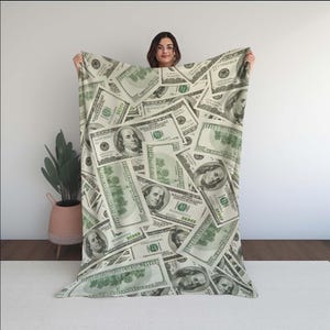 Può includere: Una coperta verde e bianca con un motivo di banconote in dollari americani. La coperta è realizzata in tessuto morbido e confortevole e presenta un motivo ripetitivo di banconote da $ 100.