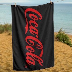 May include: Black beach towel with the red Coca-Cola logo printed vertically down the centre.