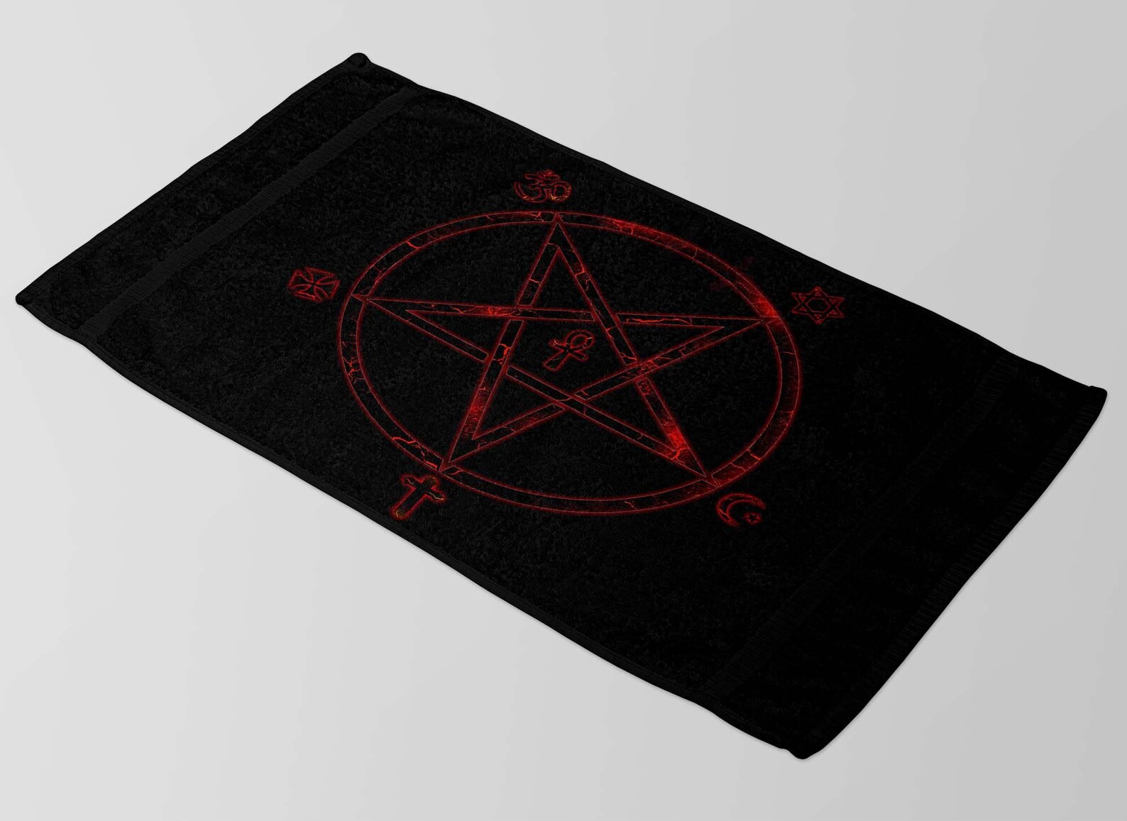 Flat lay of black occult beach towel with red pentagram and mystical symbols, displayed on light gray surface.